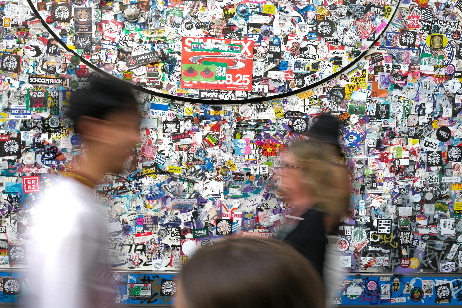 people walking past wall of logo collage